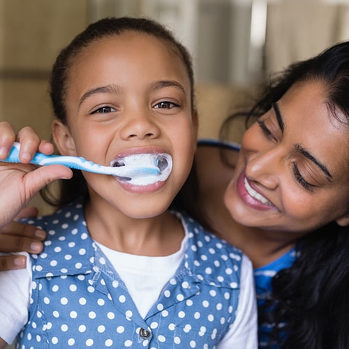 Mother watching her young daughter brush her teeth 