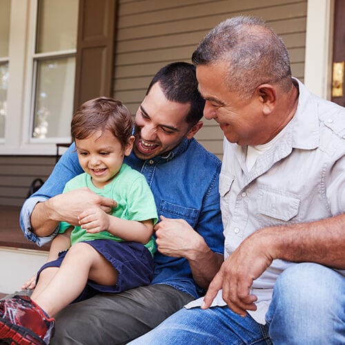Grandfather, son and grandson sitting on porch steps laughing
