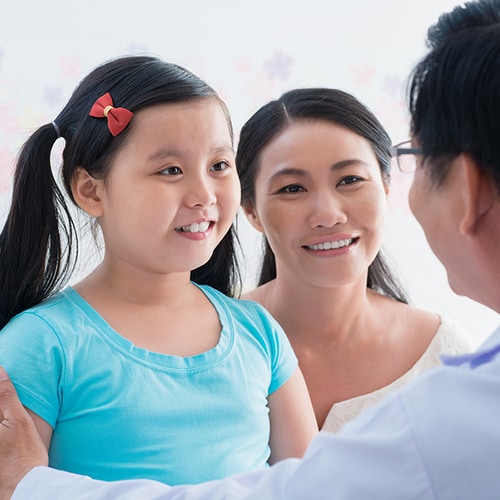 pediatric dentist talking to young patient as her mother listens in