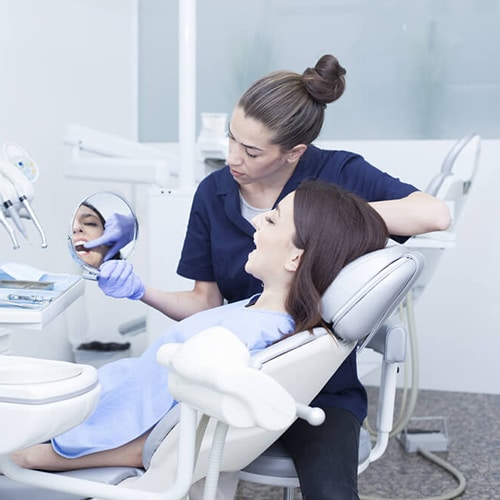 Nurse holding handheld mirror to allow patient to look at her teeth in treatment room