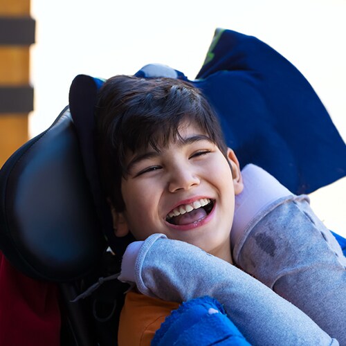 Smiling child in his wheelchair with support pillows around his neck 