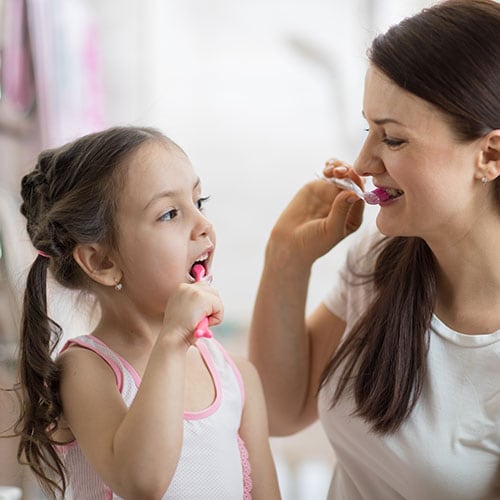 Mother teaching her daughter how to brush her teeth