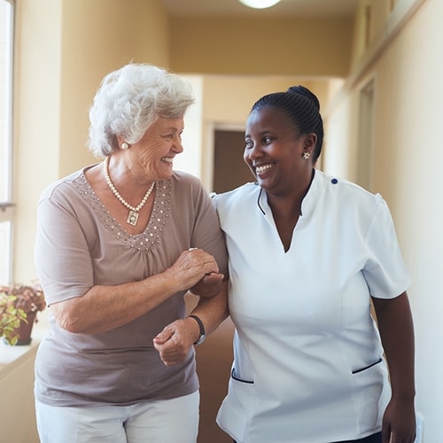 A patient and nurse walking down the hall with arms locked while smiling 