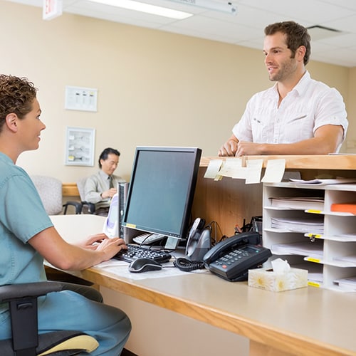 Nurse sitting down using a computer as a patient talks to her over the desk
