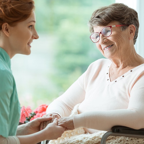 Elderly woman wearing glasses and in wheelchair holding hands with a younger woman